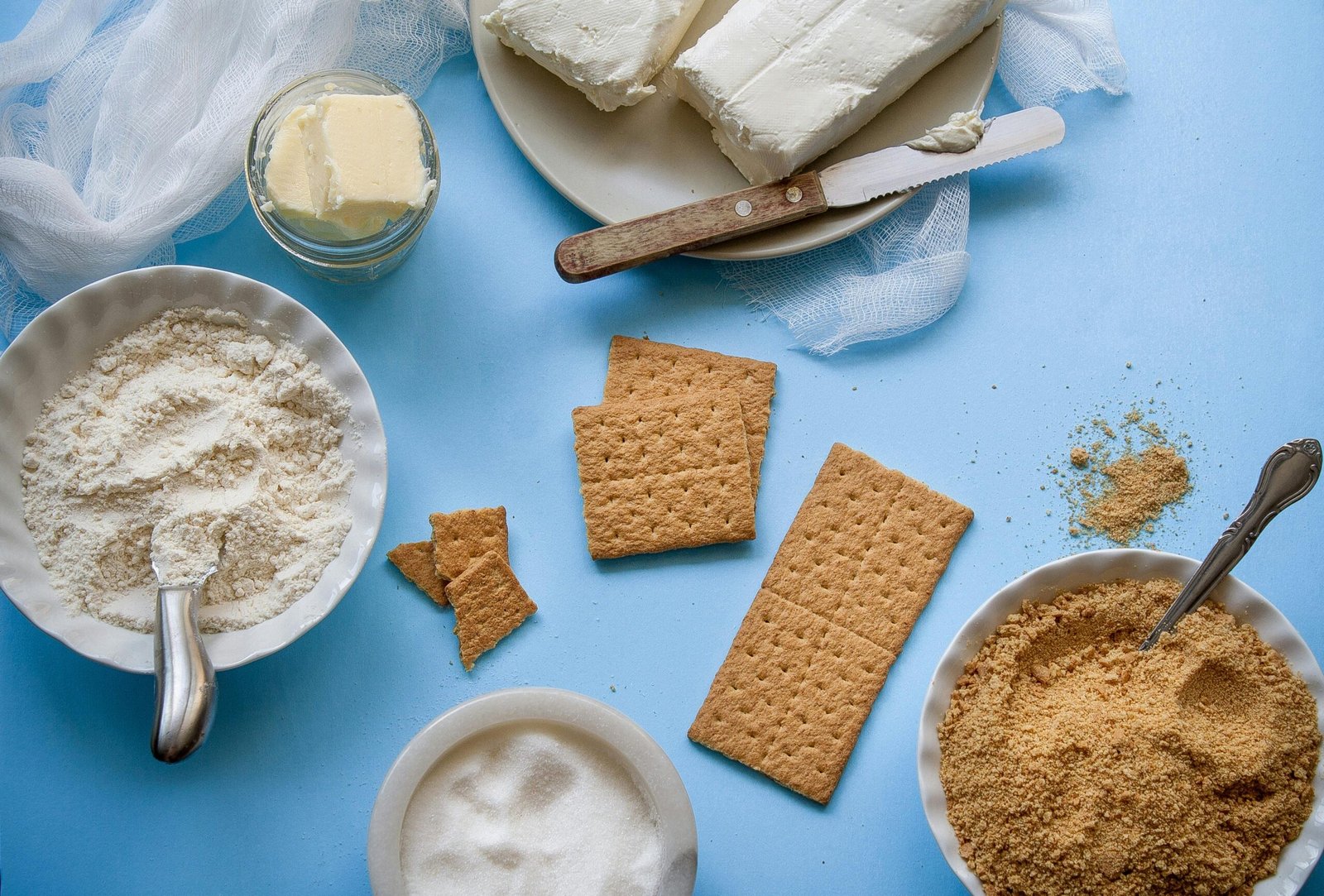 Flat lay of baking ingredients including crackers, butter, and flour on a blue background.