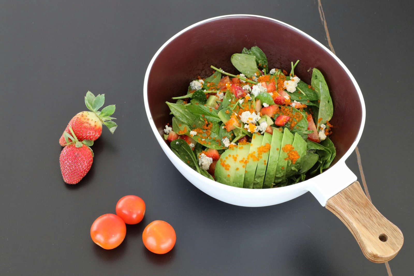 Delicious spinach salad with avocado, strawberries, tomatoes, and blue cheese crumbles.