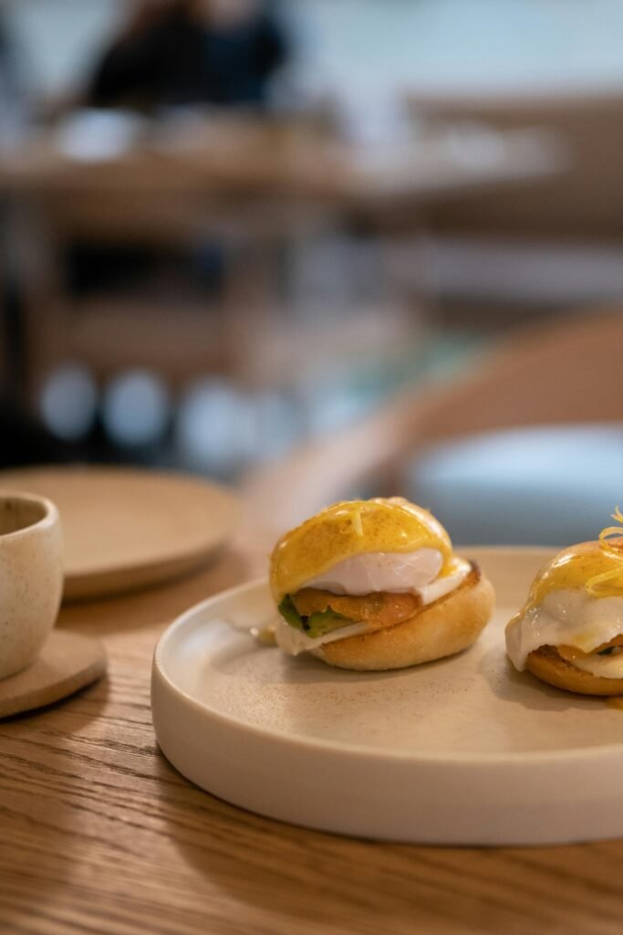 A close-up of two eggs benedict on a white plate in a stylish cafe setting.