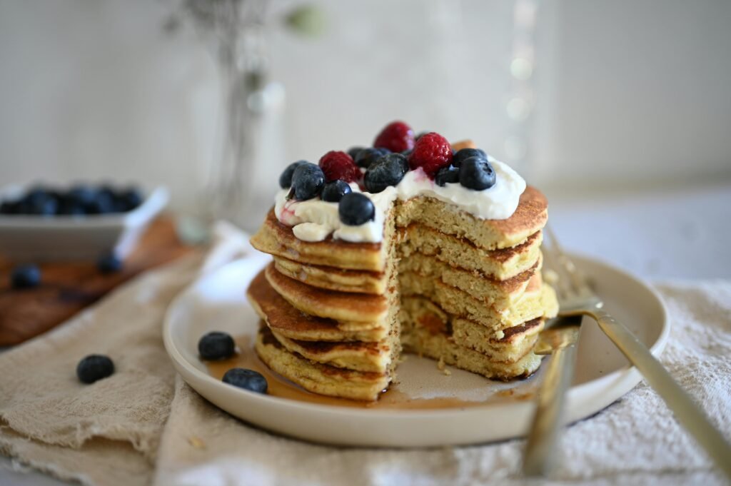 Stack of pancakes topped with blueberries and raspberries on a plate with syrup.