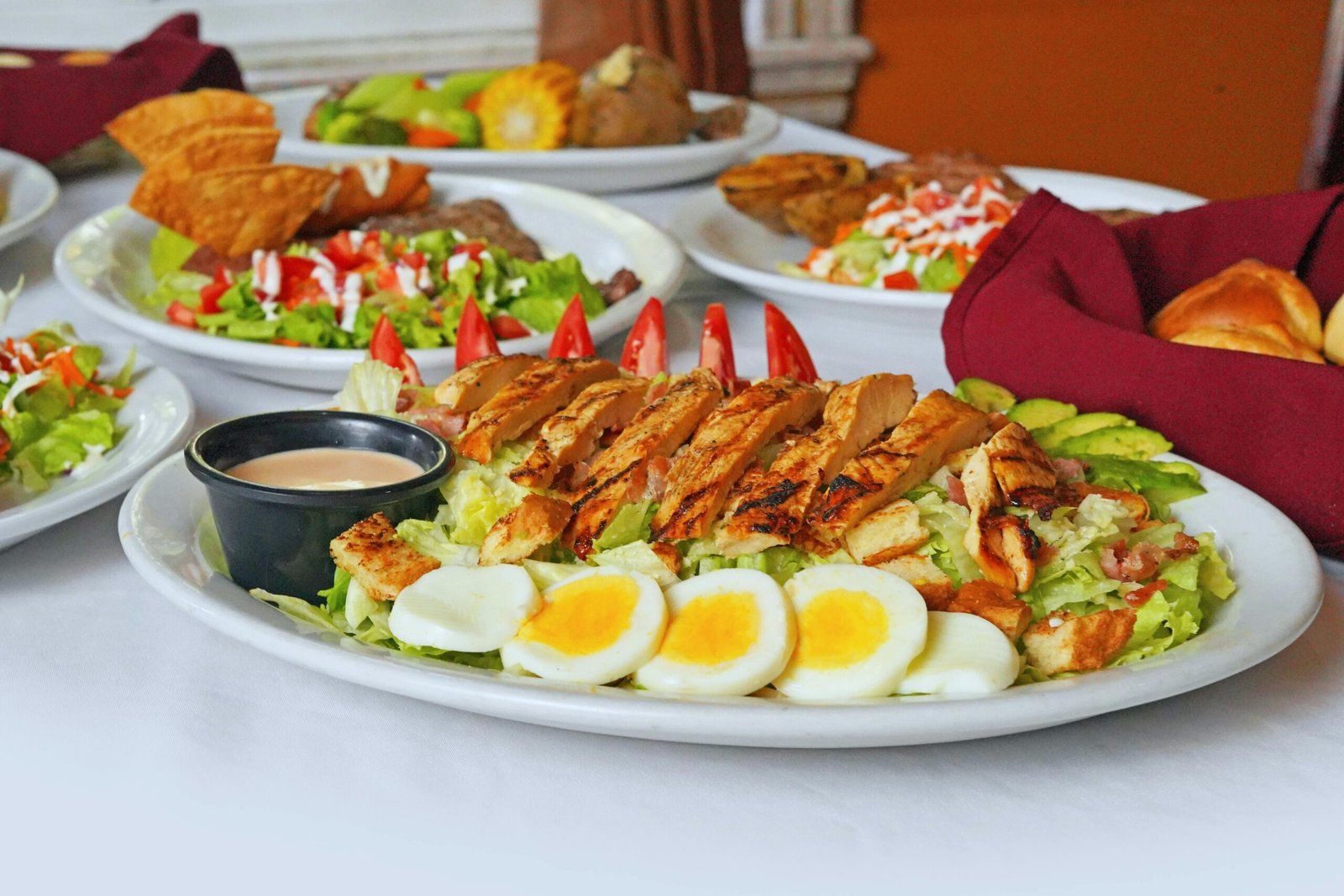 A vibrant plate of grilled chicken and Cobb salad with boiled eggs and sides on a dining table.