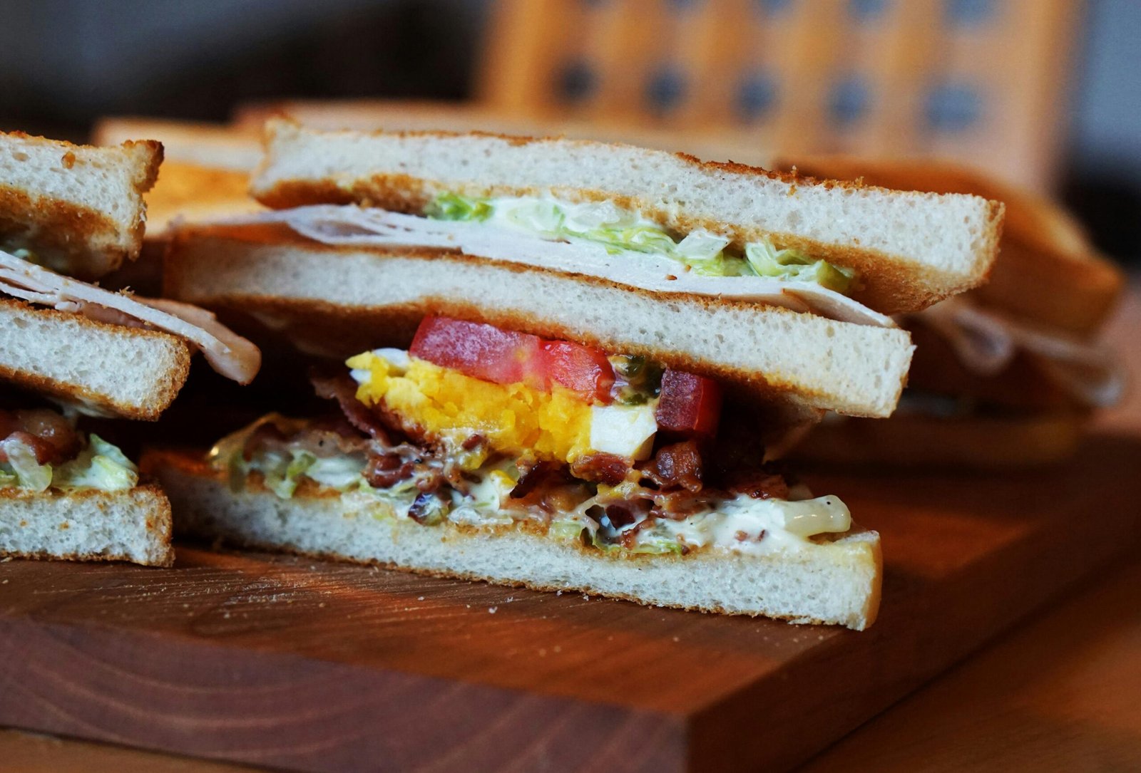 Close-up of a sandwich with egg, bacon, and fresh vegetables on a wooden board.