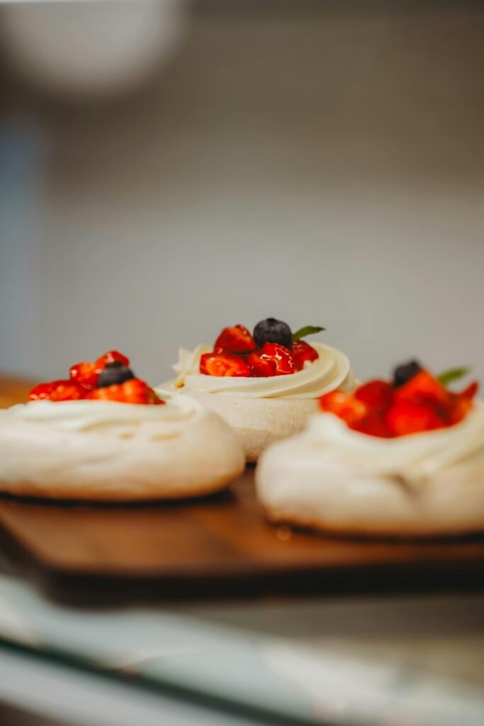 Close-up of homemade mini pavlovas topped with fresh berries on a wooden board. easy pavlova recipe