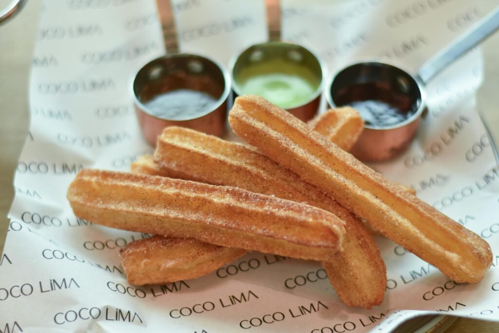 Close-up of crispy churros with dipping sauces on branded paper, perfect sweet dessert. Easy Churros Recipe