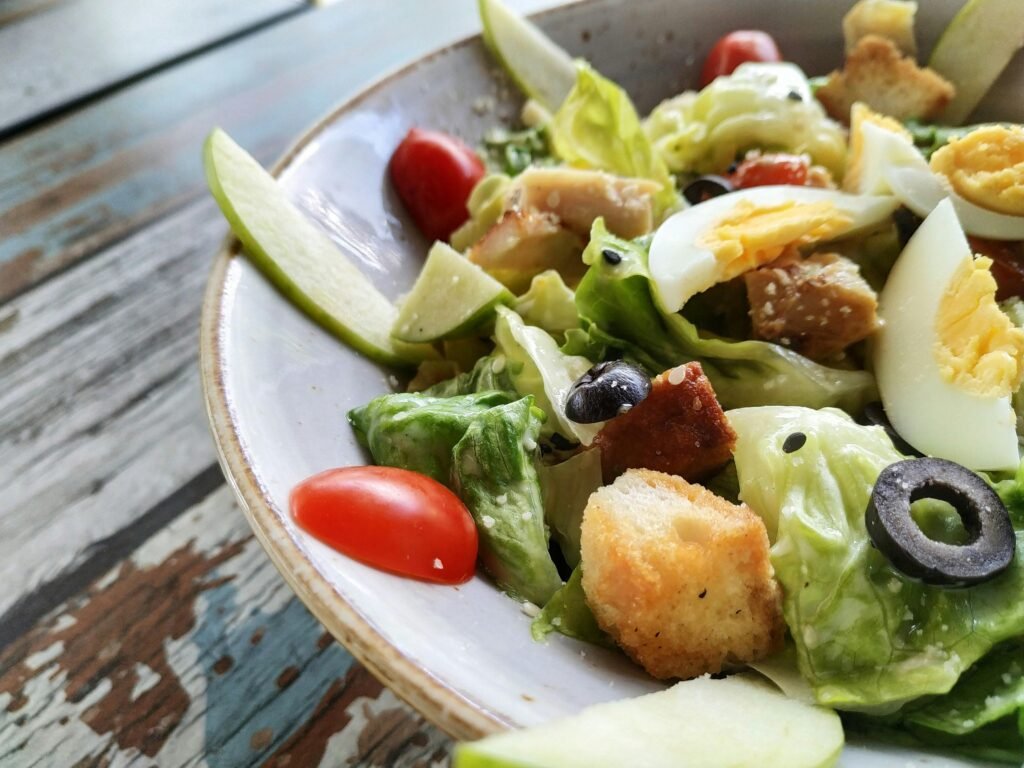 A close-up of a Caesar salad featuring fresh lettuce, eggs, croutons, and olives on a rustic table .Classic Caesar Salad Recipe