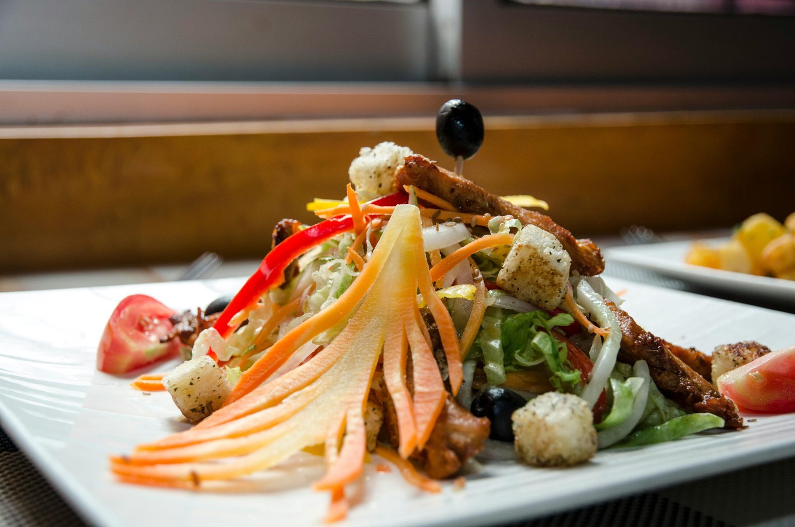 Appetizing healthy salad with fresh vegetables and fried chicken decorated with black olives and served in white plate