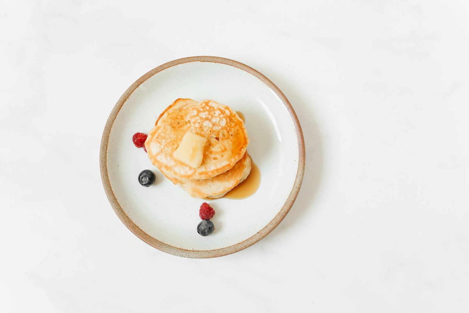 Artfully arranged pancakes with syrup, butter, and fresh berries on a white plate.