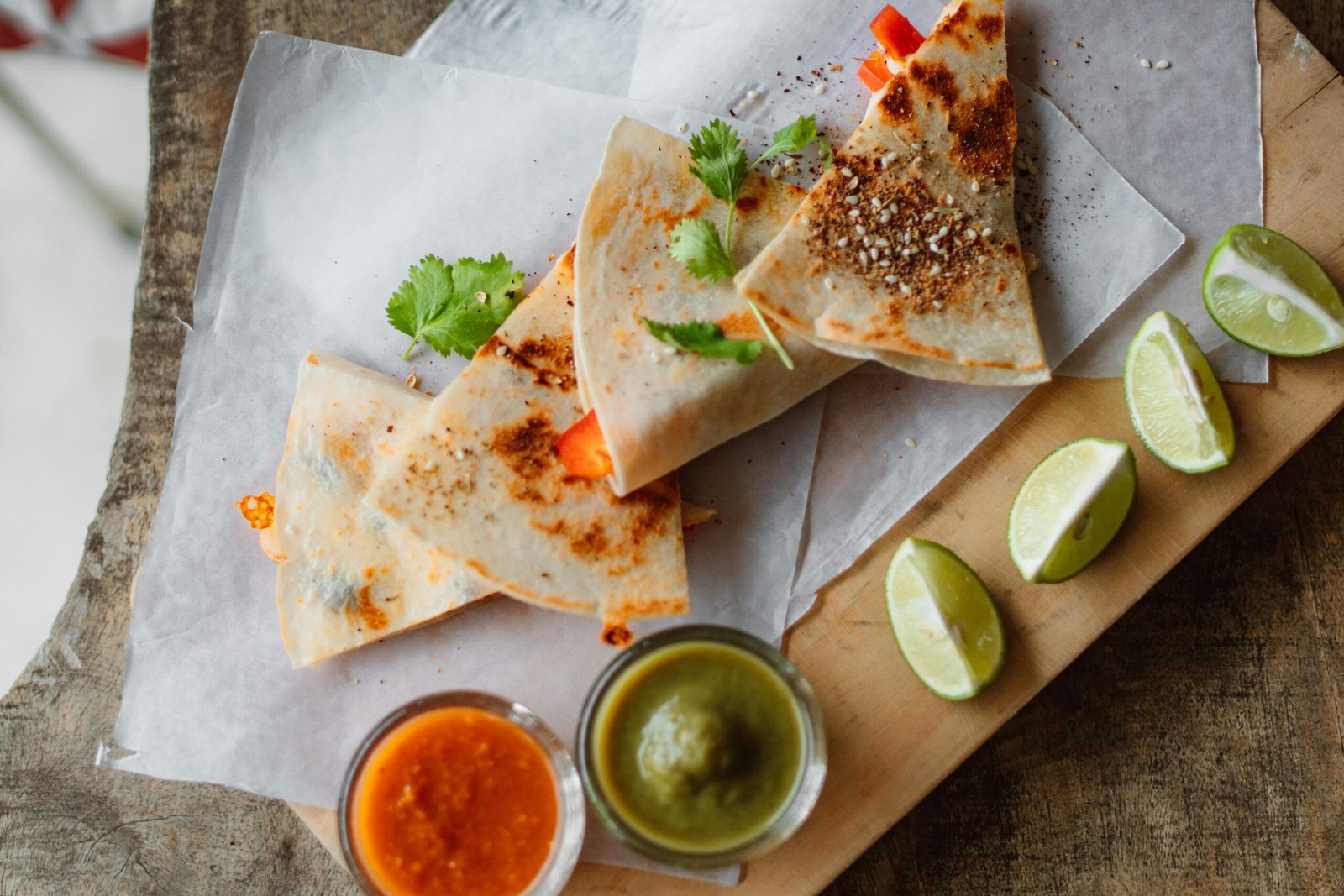 Top view of quesadillas served with salsa and lime slices on rustic paper.