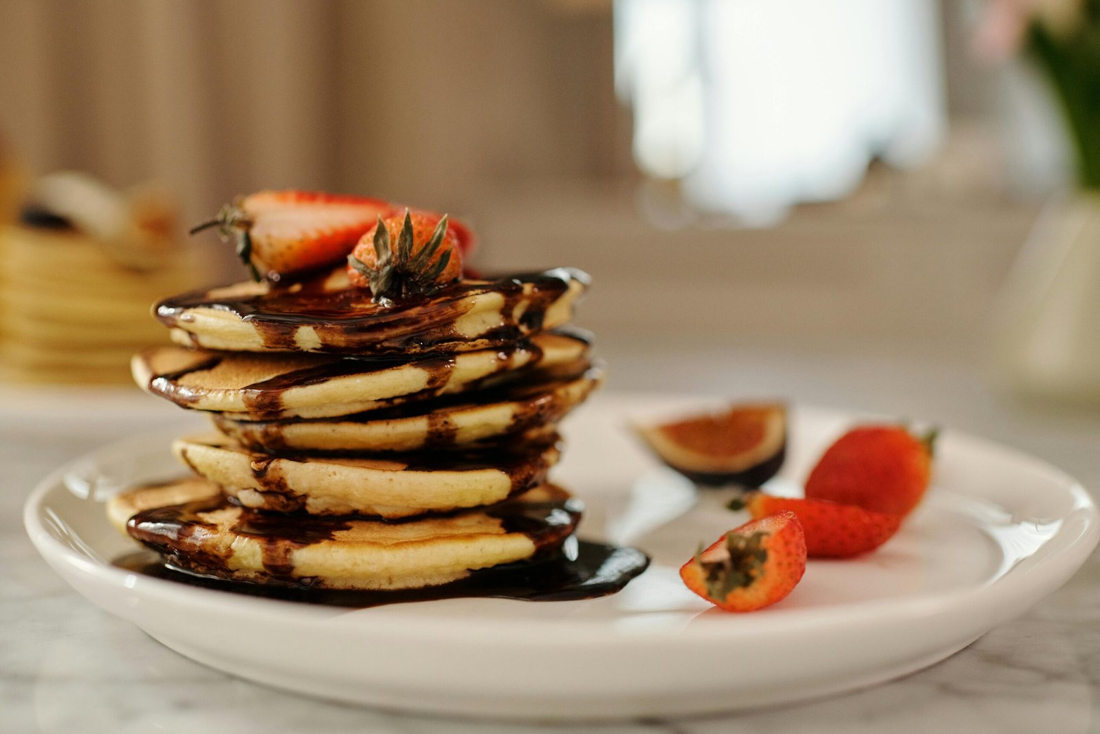 Close-up of a stack of pancakes drenched in chocolate syrup, topped with strawberries for a delicious breakfast.