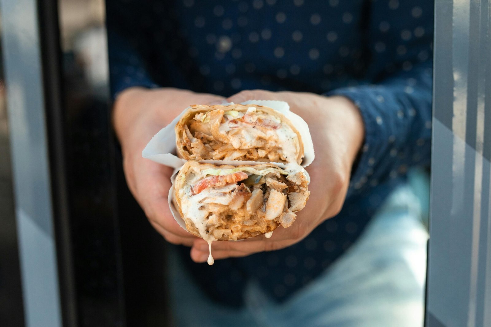 Delicious chicken shawarma held by hand, wrapped with fresh ingredients.