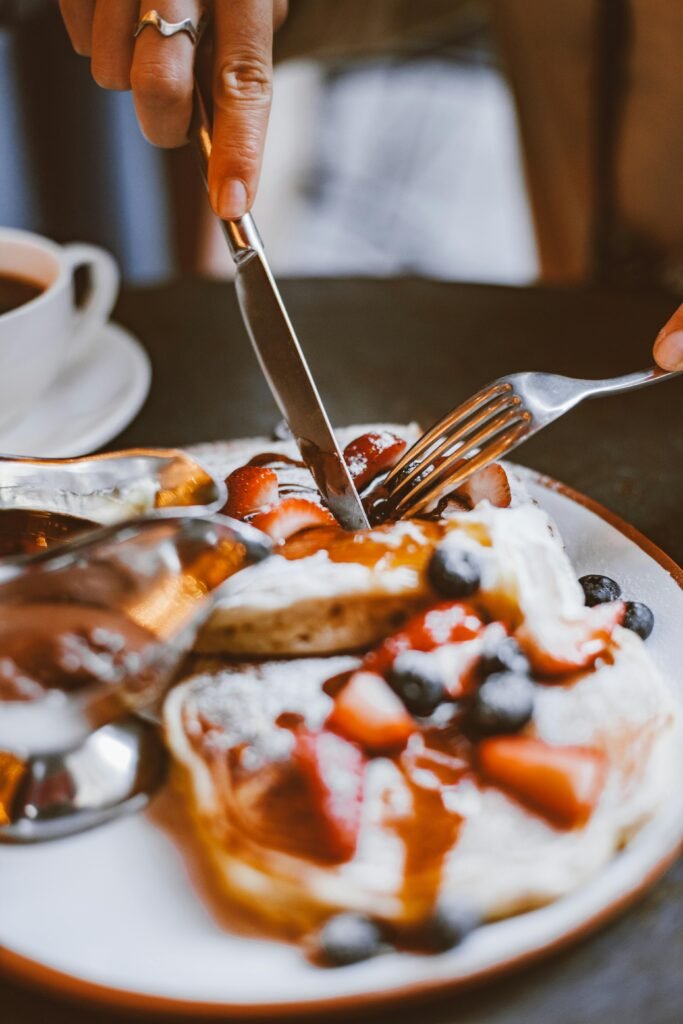 Close-up of pancakes topped with fresh berries and syrup, being sliced with a knife and fork.