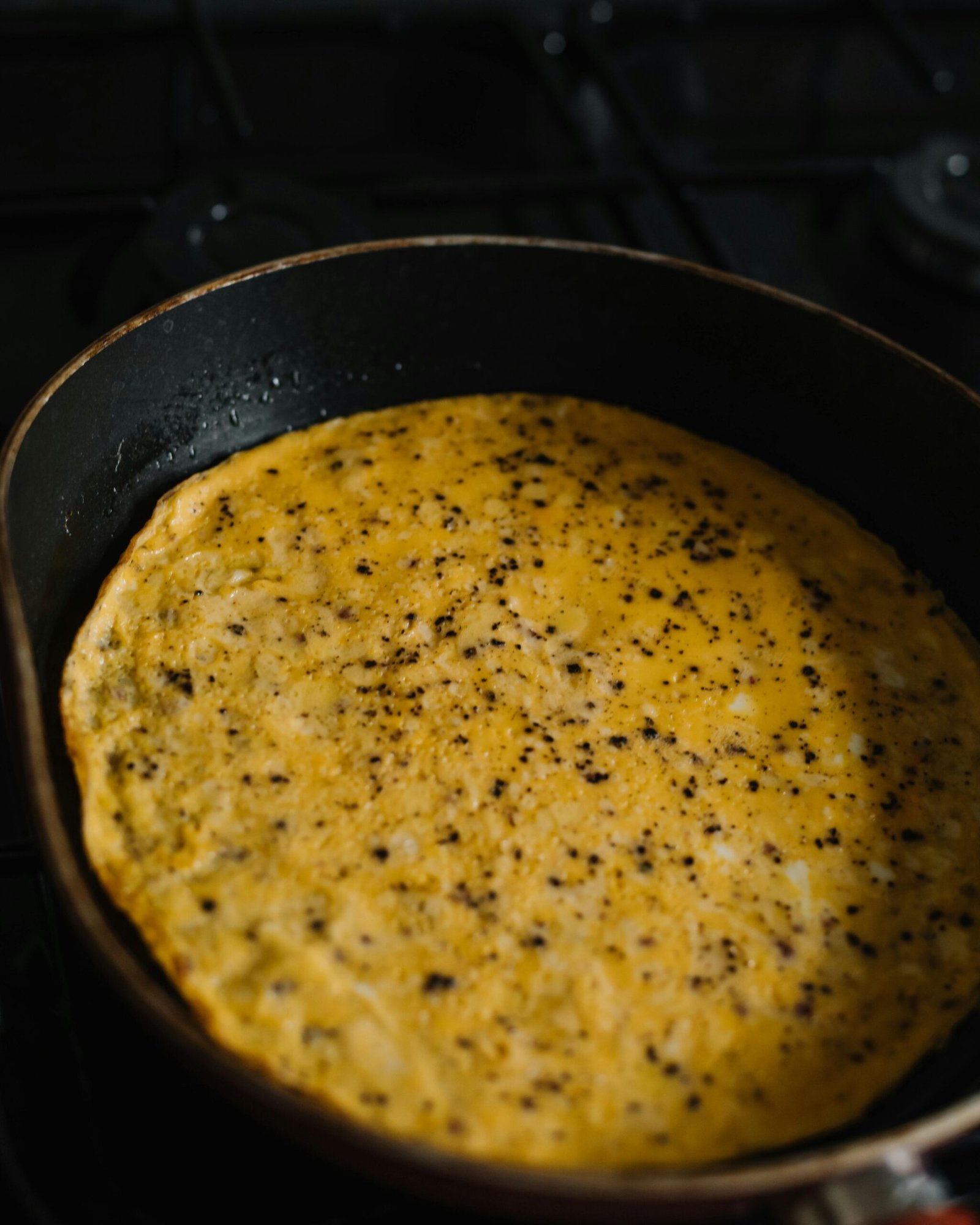 A close-up view of a seasoned omelette cooking in a frying pan, highlighting its texture and spices.