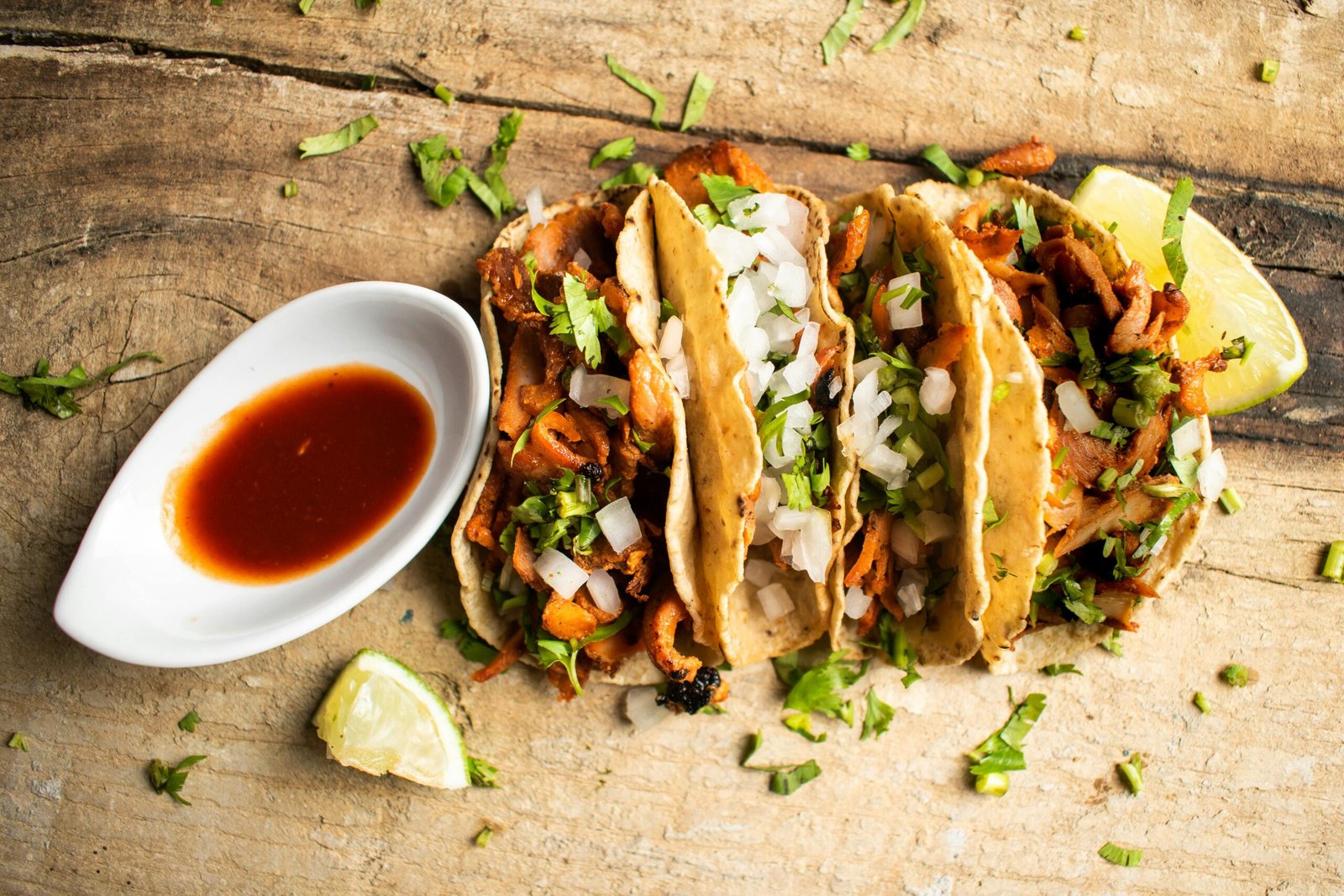 Close-up of three tacos al pastor with cilantro and onion, served with salsa on a rustic table.