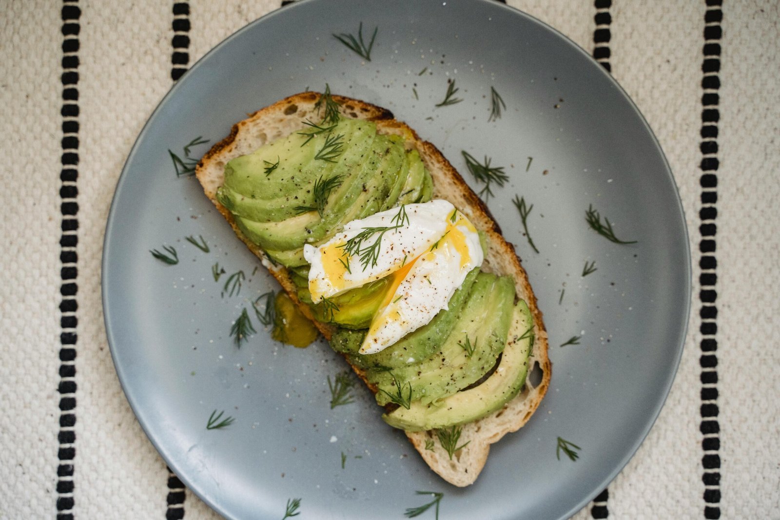 Elegant avocado toast with poached egg and fresh dill on gray plate, perfect for gourmet breakfast.