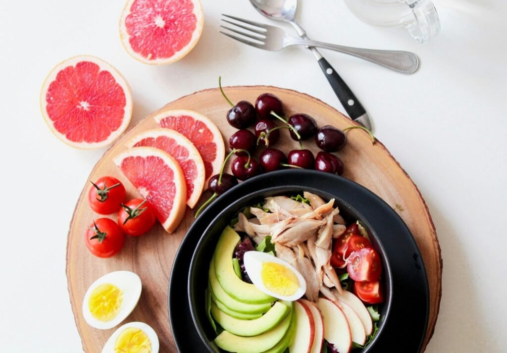 A vibrant breakfast flat lay featuring a mix of fruits, avocado, eggs, tomatoes, and sliced meats on a wooden platter. cobb salad recipe