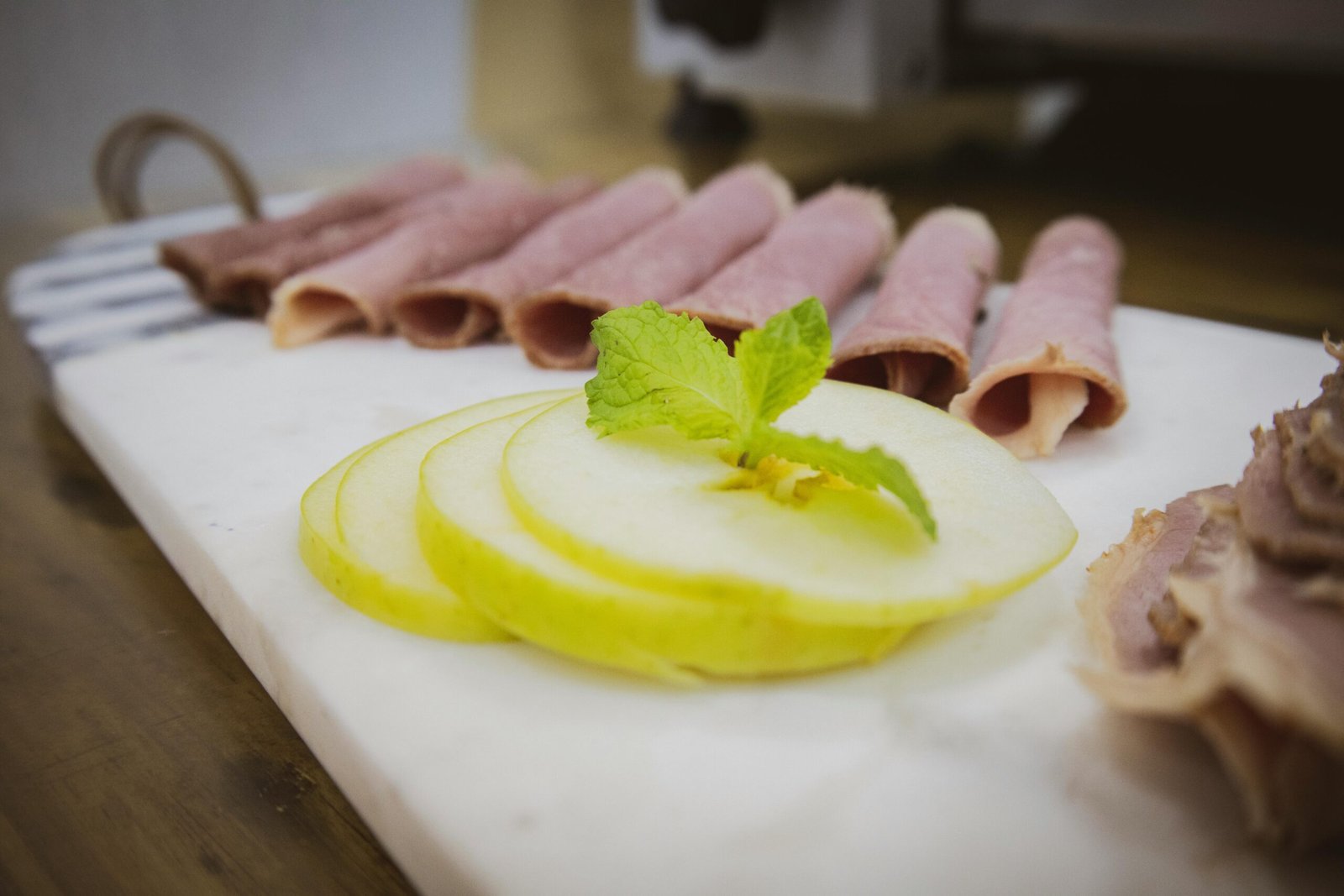 Close-up of rolled ham slices and apple slices with mint leaf garnish on a cutting board.