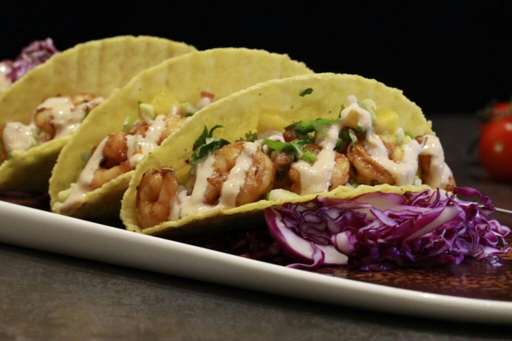 Close-up of shrimp tacos with creamy sauce and fresh vegetables on a plate, perfect for food photography.