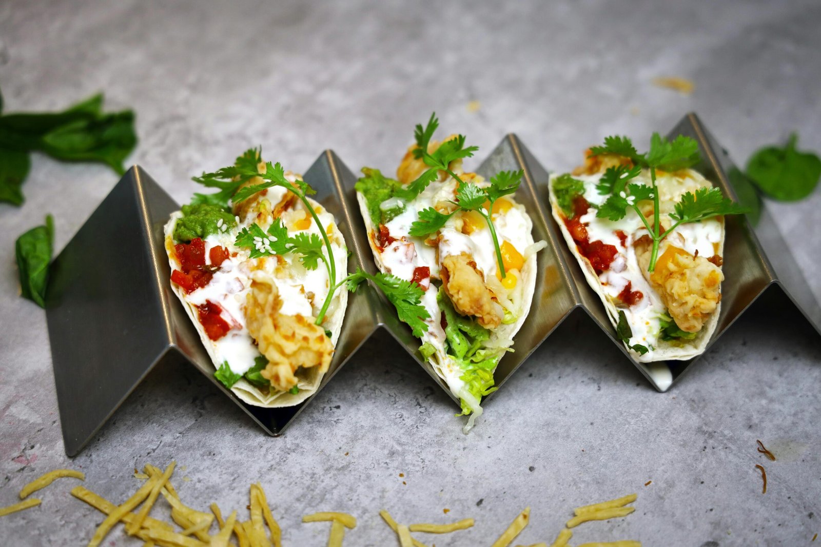 Three crispy fish tacos with creamy sauce, topped with fresh cilantro and red salsa.