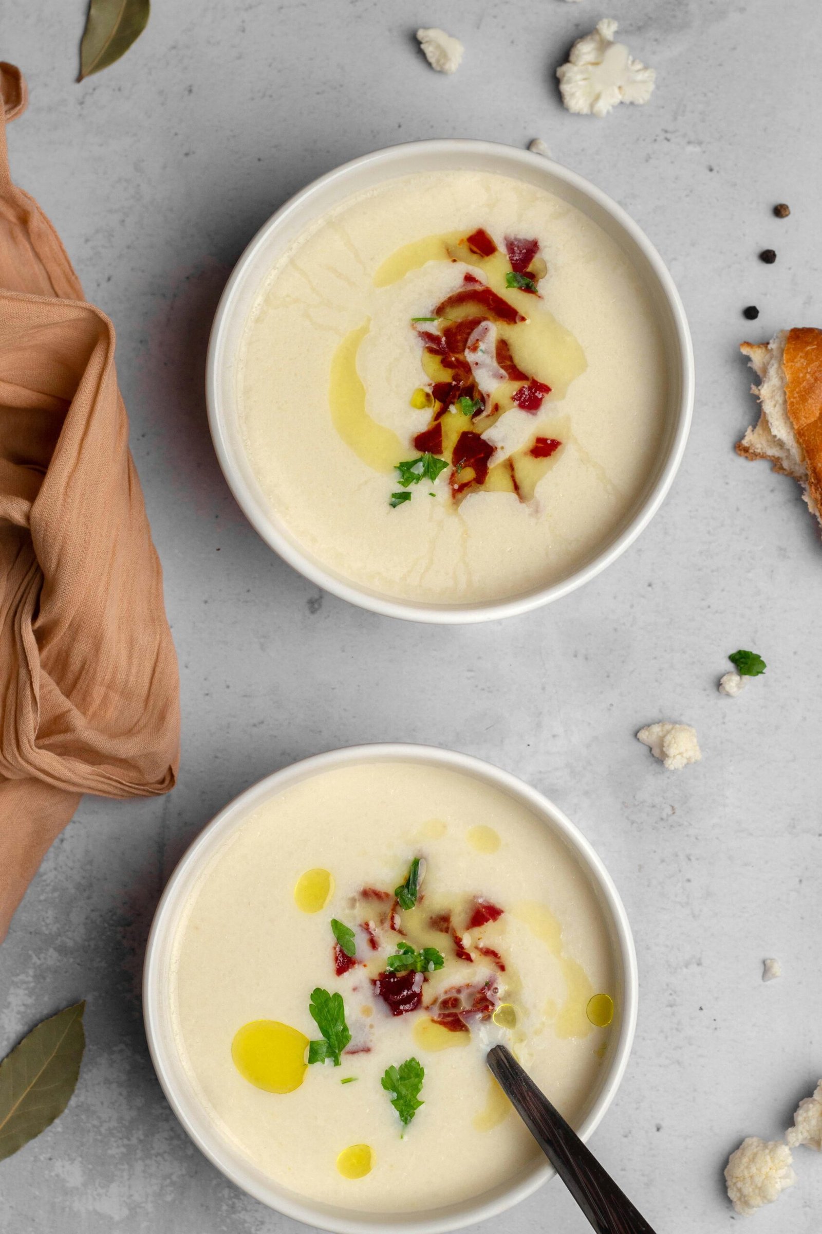 Top view of creamy cauliflower soup garnished with herbs and spices in white bowls.