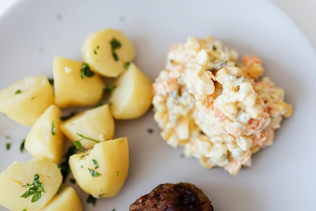 A delectable plate of potato salad with herbs, served alongside boiled potatoes and a meatball, perfect for dinner. slow cooker mashed potato recipe