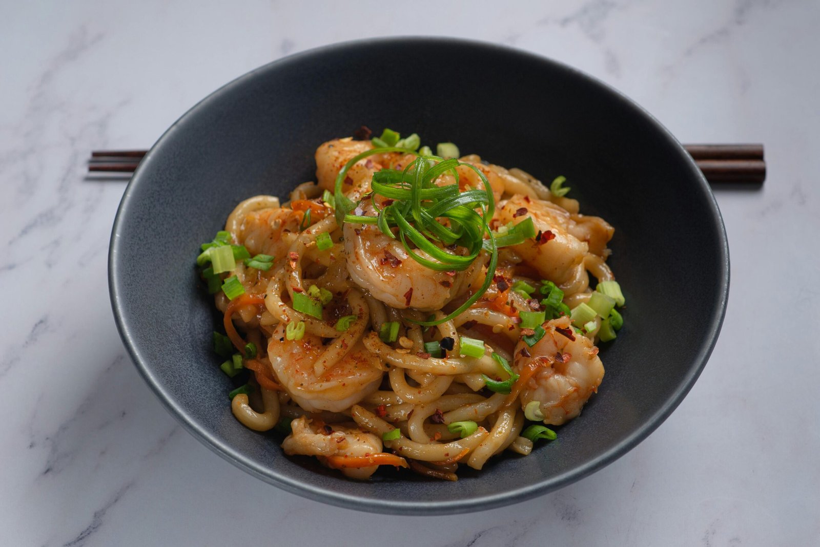 A mouth-watering dish of shrimp udon noodles garnished with scallions and chili flakes.